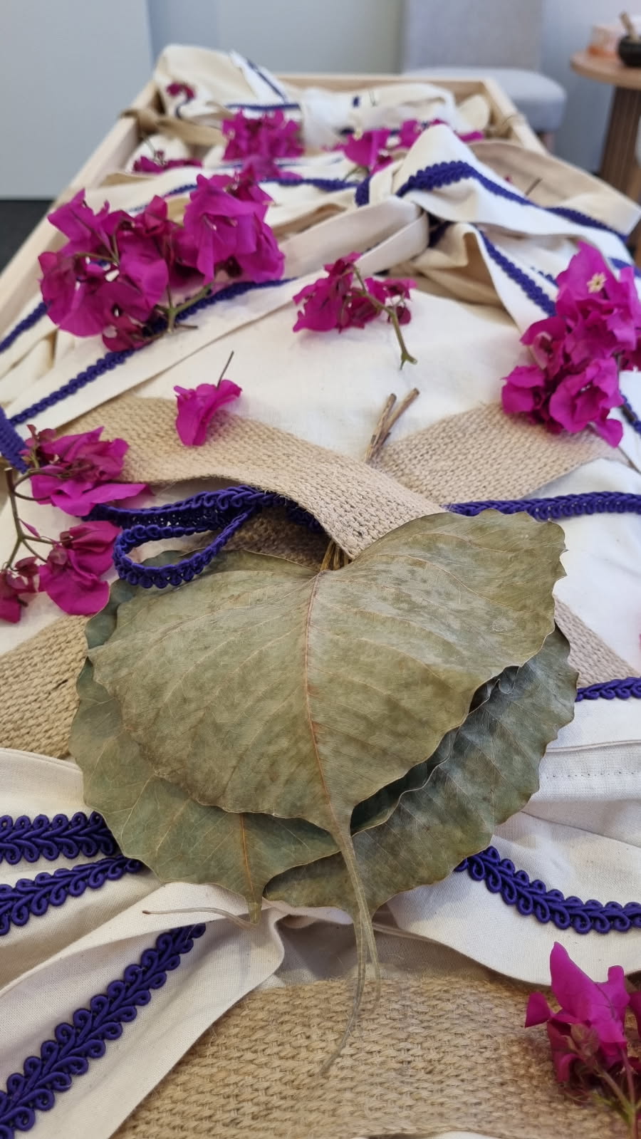 Casket draped with white fabric and purple trim, adorned with bright pink flowers and a large dried leaf centerpiece for a funeral tribute